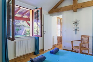 A bedroom with a bed, a chair, a window with curtains, and a door leading to another room.