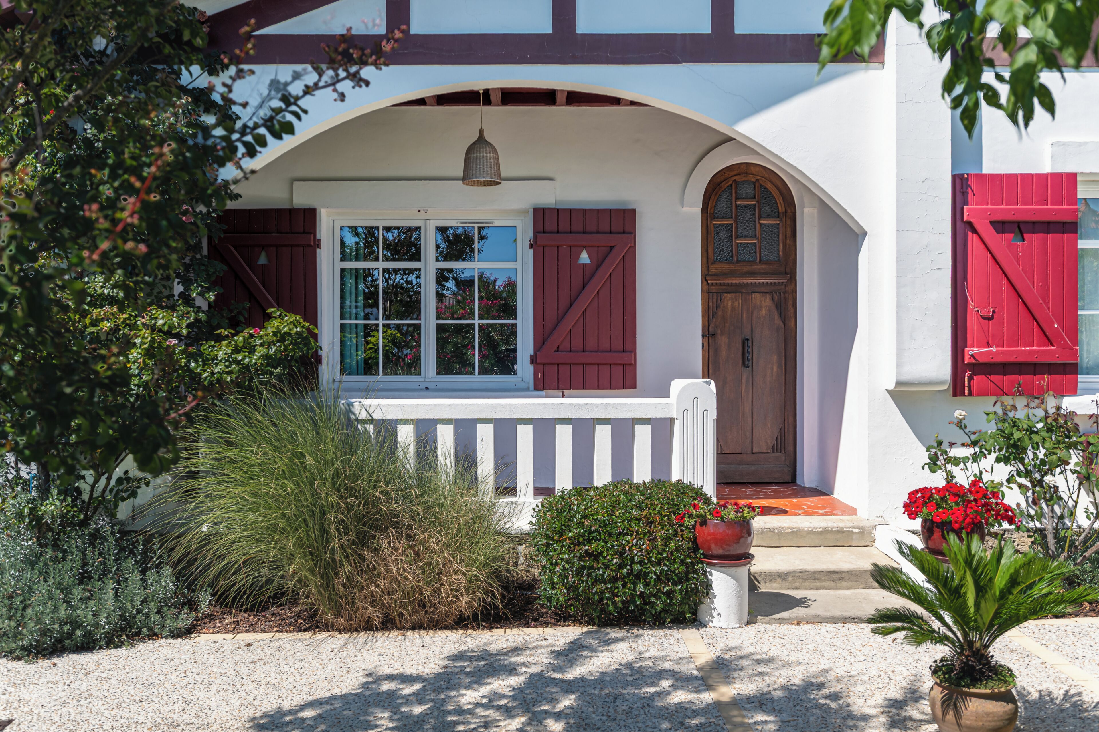 A house with a white exterior, a wooden porch, a red door, and a window with shutters.