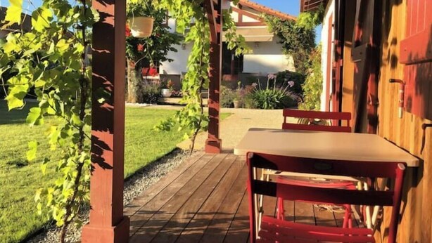 Een houten pergola met een tafel en stoelen, omringd door groen en een verzorgd gazon.