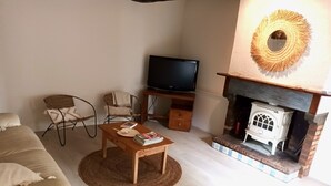 A living room with a sofa, a coffee table with books, a TV, a fireplace, and a chair. - Gîte Tranquille Avec Piscine Partagée (Crespin)