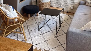 A modern living room with a white brick wall, a large painting, a wicker lamp, and a grey sofa. - Rooftop Mirabeau • Private Roof Terrace • A/C • 2 Bedrooms (Aix-en-Provence)