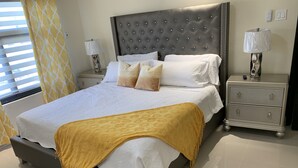 A modern hotel room with a large bed, two bedside tables, and a nightstand. - Sunshine Oasis @Pyramid Point (ocho rios)
