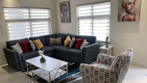 A modern living room with a sectional sofa, a patterned armchair, a coffee table, and a small side table with a cactus. - Sunshine Oasis @Pyramid Point (ocho rios)