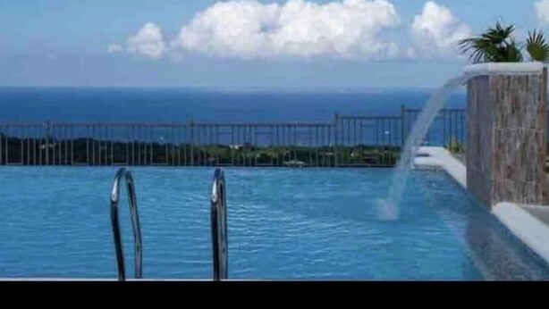 A swimming pool with a view of the ocean and a distant shoreline. - Sunshine Oasis @Pyramid Point (ocho rios)
