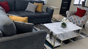 A modern living room with a grey sofa, a patterned armchair, and a white coffee table. - Sunshine Oasis @Pyramid Point (ocho rios)