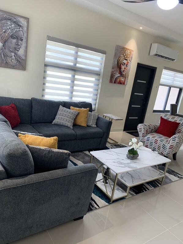Un moderno salón con un sofá gris, un sillón estampado y una mesa de centro blanca.