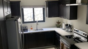 A modern kitchen with dark cabinetry, a stainless steel refrigerator, a built-in oven, and a window providing natural light. - Sunshine Oasis @Pyramid Point (ocho rios)