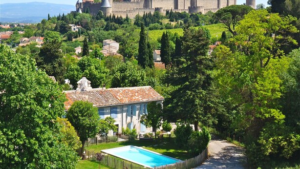 A castle on a hill with a swimming pool and a villa in the foreground.