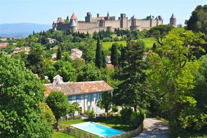 Un château perché sur une colline, avec une piscine et une villa au premier plan.