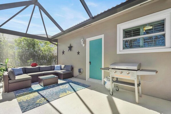 A covered patio with a sectional sofa, a grill, and a door with a star decoration.