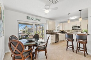 Een keuken met een eethoek, een plafondventilator en een bordje met de tekst 'BEACH HOUSE'.