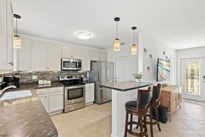 A modern kitchen with white cabinetry, stainless steel appliances, and a central island with bar stools.