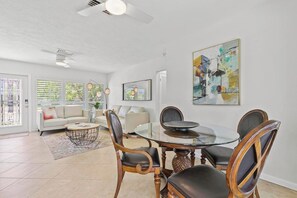A modern living room with a glass dining table, leather chairs, a white sofa, and artwork on the walls. - Rose Court-Charming 2 BDR Waterfront Bungalow (Marco Island)