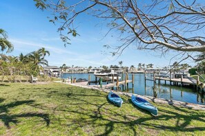 A marina with boats docked, a grassy area with kayaks, and a clear sky. - Rose Court-Charming 2 BDR Waterfront Bungalow (Marco Island)