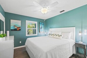 A bedroom with a bed, ceiling fan, artwork, and a nightstand with a lamp. - Rose Court-Charming 2 BDR Waterfront Bungalow (Marco Island)
