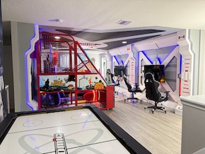 A gaming room with a large screen, gaming chairs, and a red play structure.