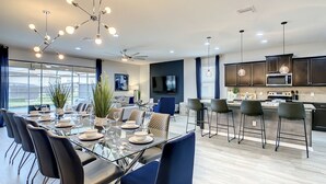 A modern dining area with a glass table, black and blue chairs, and a ceiling fan. - Star Wars 8BR | Arcade Game Rm | 2 Theaters | Pool (Kissimmee)