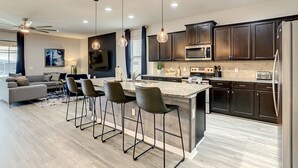 A modern kitchen with dark cabinetry, stainless steel appliances, and a central island with bar stools. - Star Wars 8BR | Arcade Game Rm | 2 Theaters | Pool (Kissimmee)