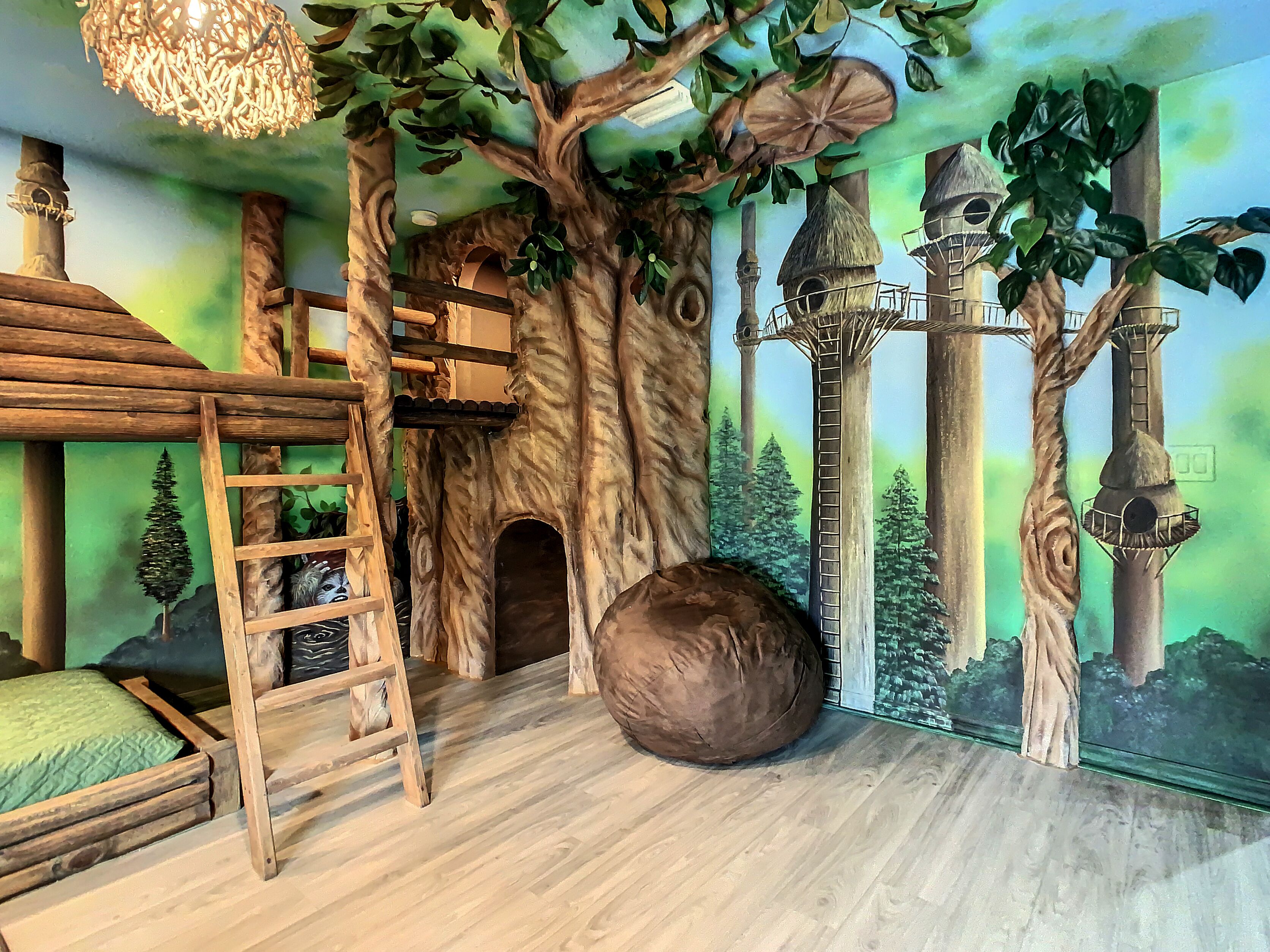 A room with a wooden bunk bed, a ladder, a large tree mural, and a forest scene on the wall.