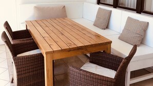 Ein Holztisch mit vier Stühlen, ein weißes Sofa mit Kissen und ein Fenster mit Jalousien.