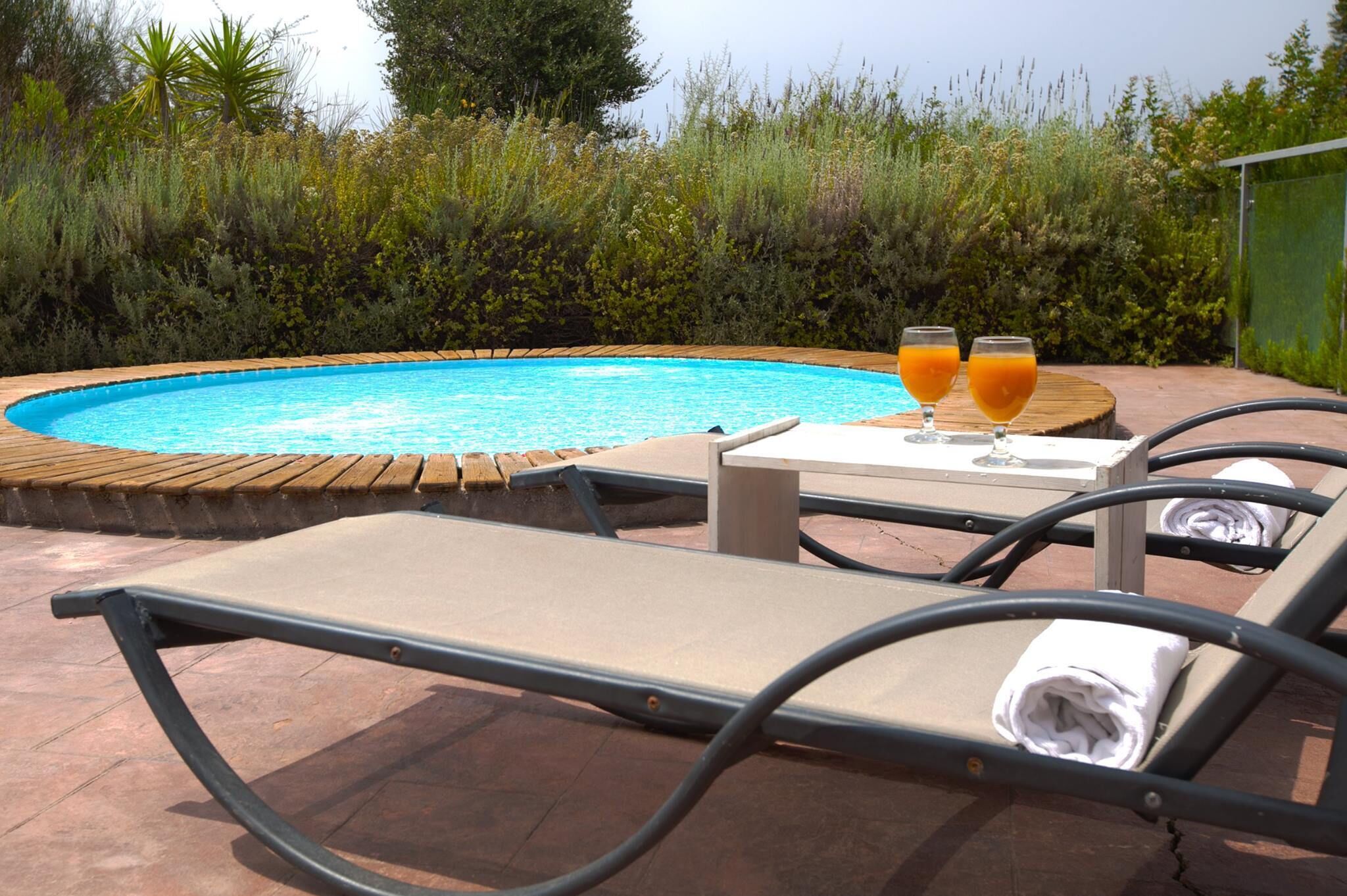 A poolside area with lounge chairs, a table with two glasses of orange juice, and a wooden deck surrounding the pool.