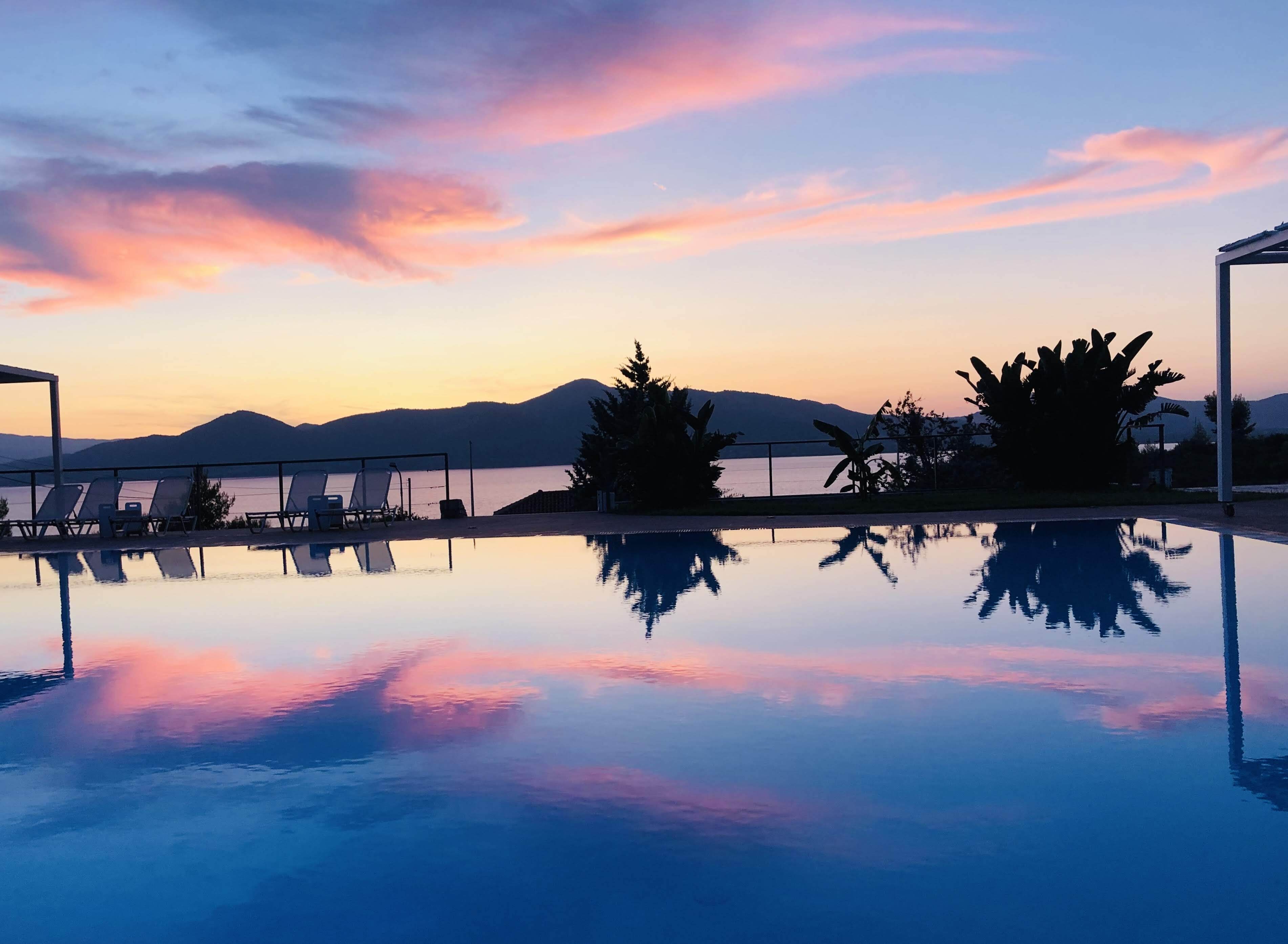 Una vista serena de la piscina al atardecer, con sillones de descanso y una vista despejada de las montañas.