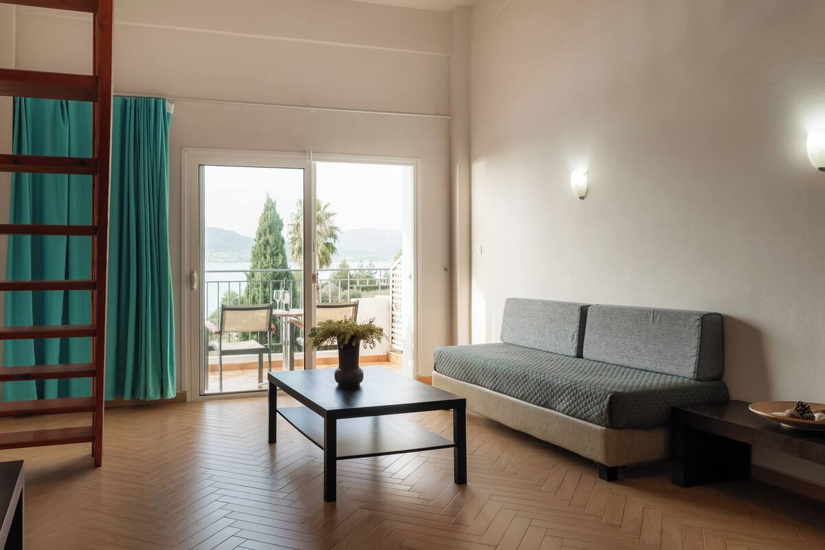 A living room with a sofa, a coffee table, a wooden floor, a balcony with a view, and a staircase.