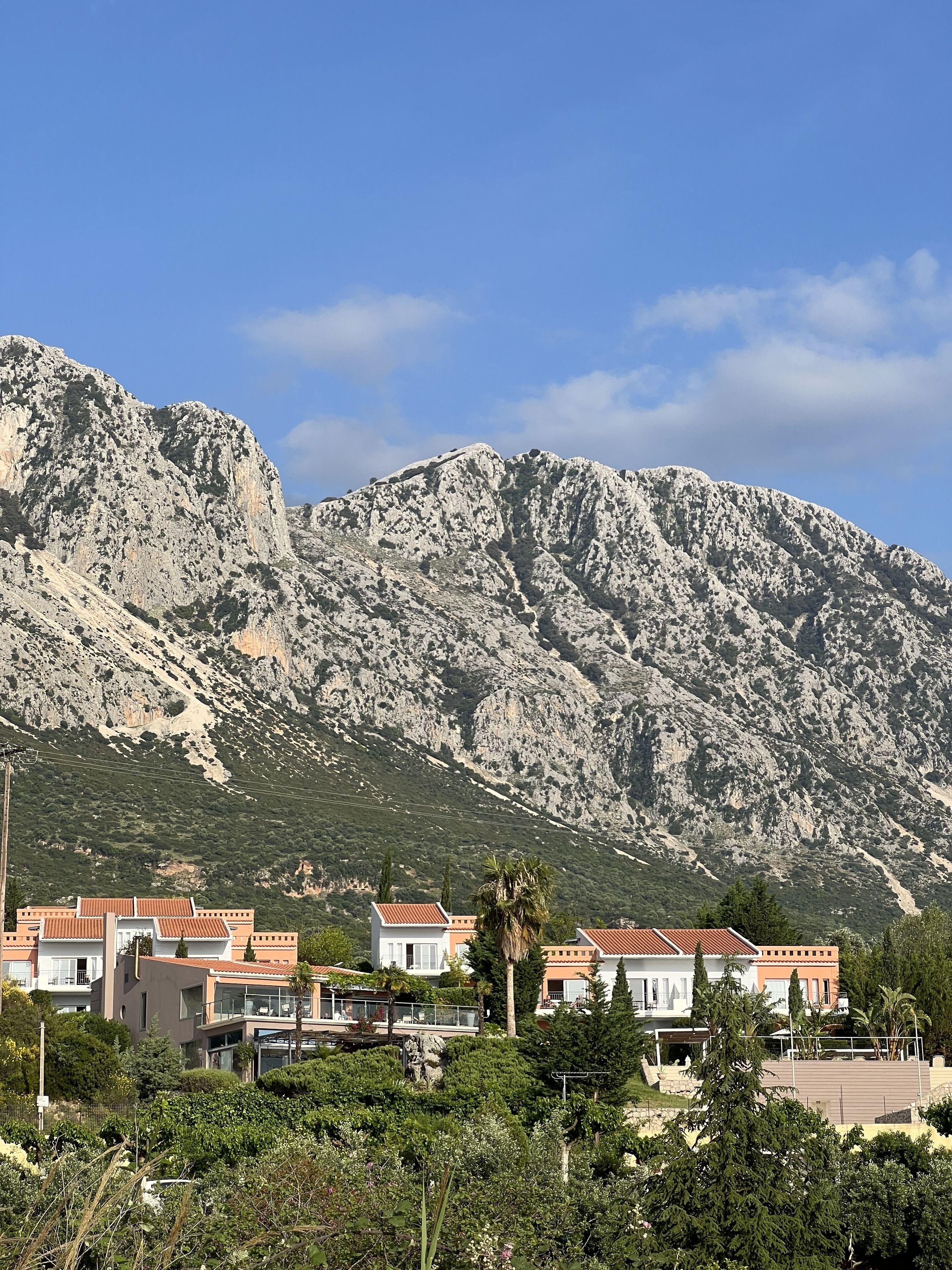 A coastal residential area with houses featuring red-tiled roofs, set against a backdrop of rocky mountains.