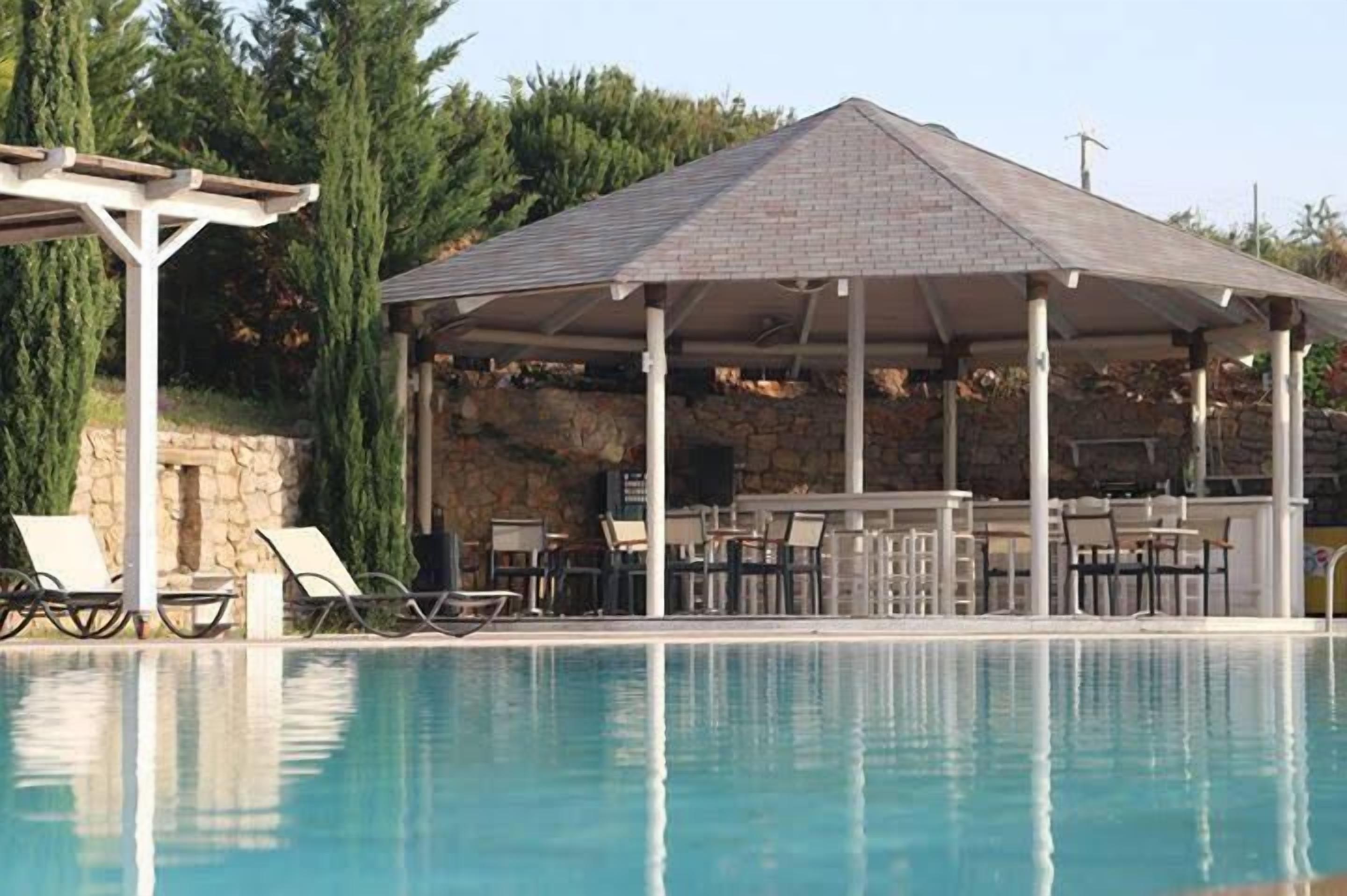 Un área junto a la piscina con zona de estar techada y sillones reclinables.