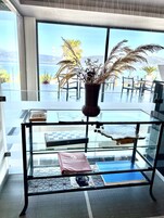 Una mesa de vidrio con un jarrón de plantas secas, libros y una bolsa rosa con la etiqueta