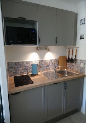 A kitchen with grey cabinets, a microwave, a sink, and a tiled backsplash. - Refurbished studio with garden and patio in the Cap Esterel holiday village (Agay)