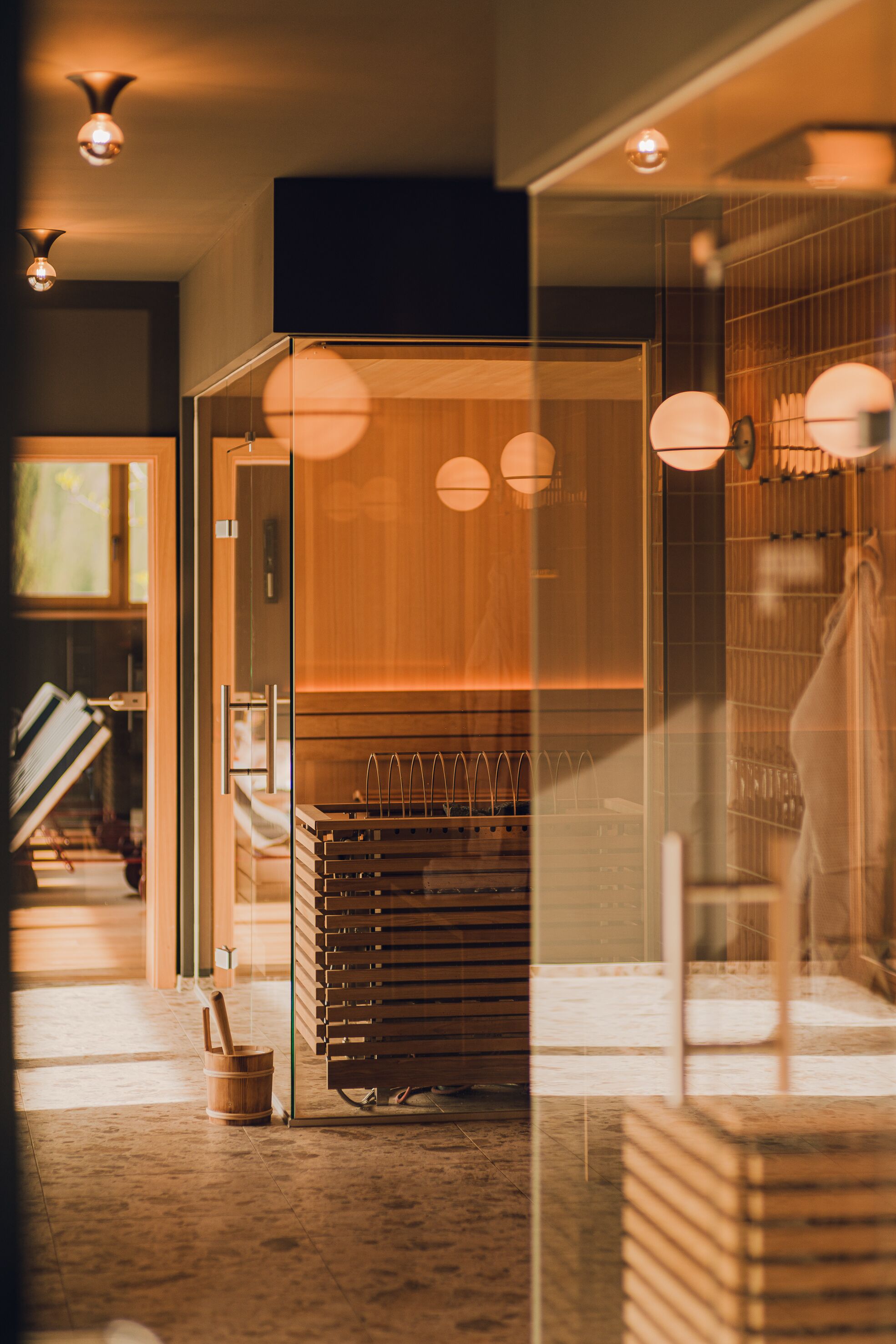 A modern interior with a glass partition, wooden furniture, and pendant lighting.