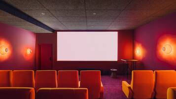 A movie theater with rows of orange seats, a large screen, and wall sconces.