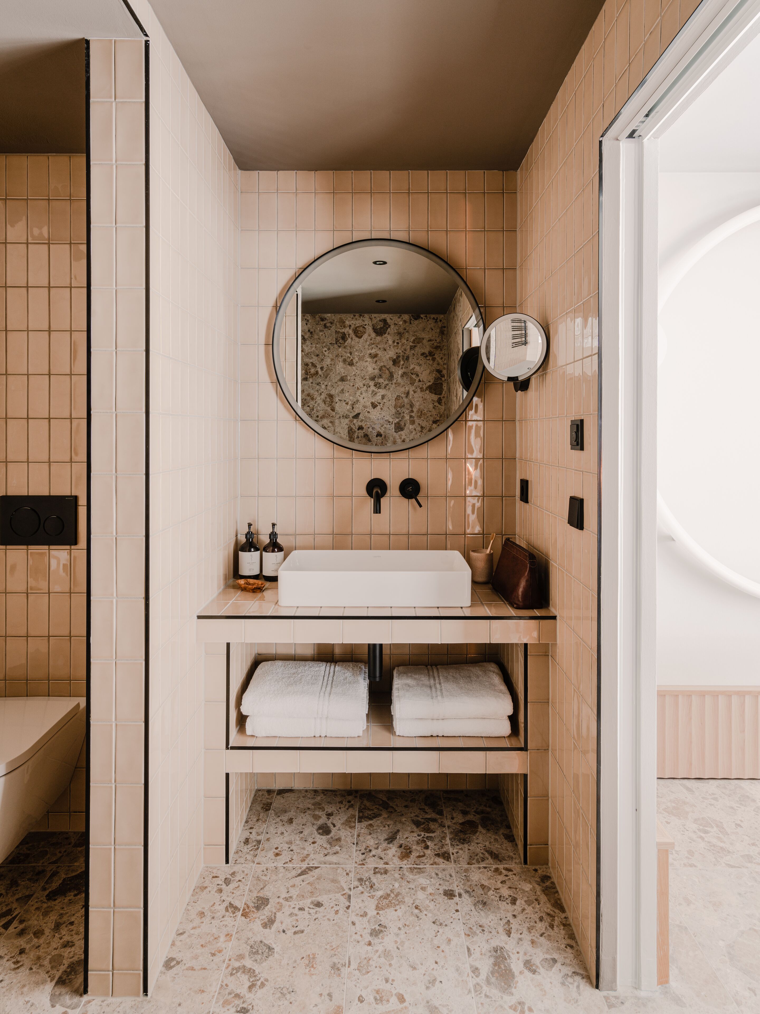 A bathroom with a freestanding sink, a round mirror, and a towel rack.
