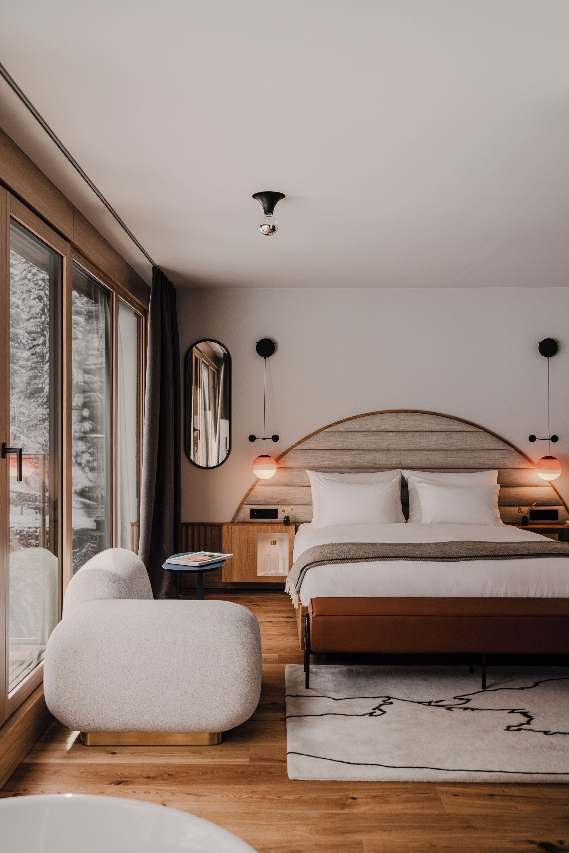 Une chambre moderne avec un grand lit, des tables de chevet, un miroir et une vue sur l’extérieur.