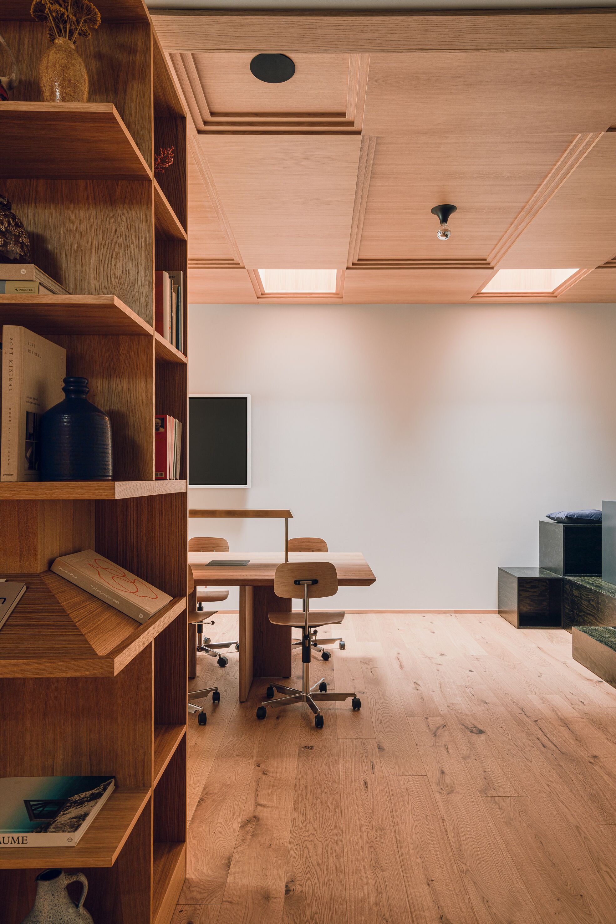 A modern office space with wooden shelving, a desk, chairs, and a large window.