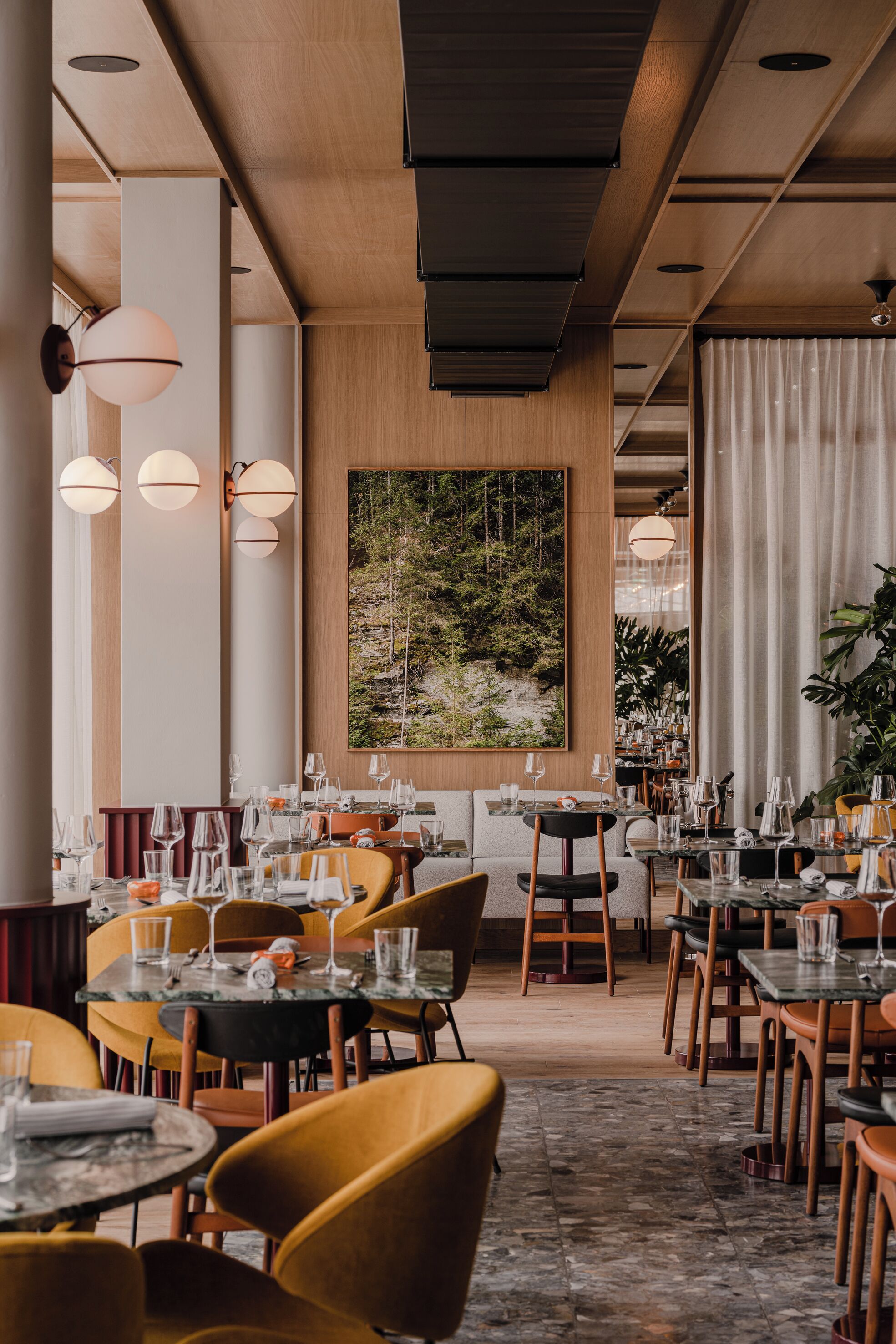 Et restaurantinteriør med flere spiseborde, stole og hængende lamper.