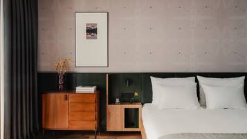 Una habitación de hotel moderna con un aparador de madera, una mesita de noche con un florero, un cuadro enmarcado en la pared y una cama bien hecha.