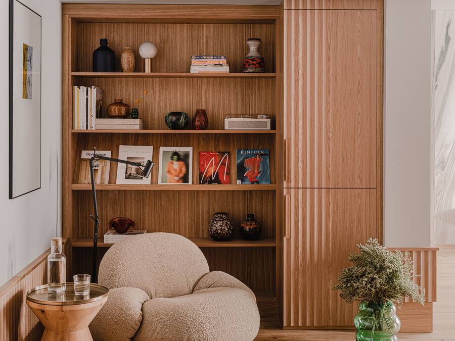 Una habitación acogedora con una estantería de madera, un sillón cómodo, una mesita auxiliar y un jarrón decorativo.
