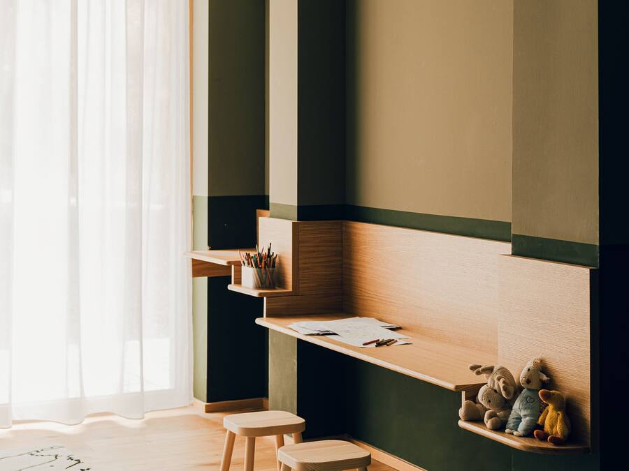 Una habitación moderna con un escritorio de madera, dos taburetes, una estantería y una alfombra.