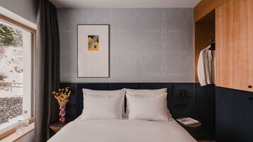 Una habitación de hotel moderna con una cama grande, una mesita de noche con un jarrón de flores, un cuadro en la pared y una ventana con cortinas.