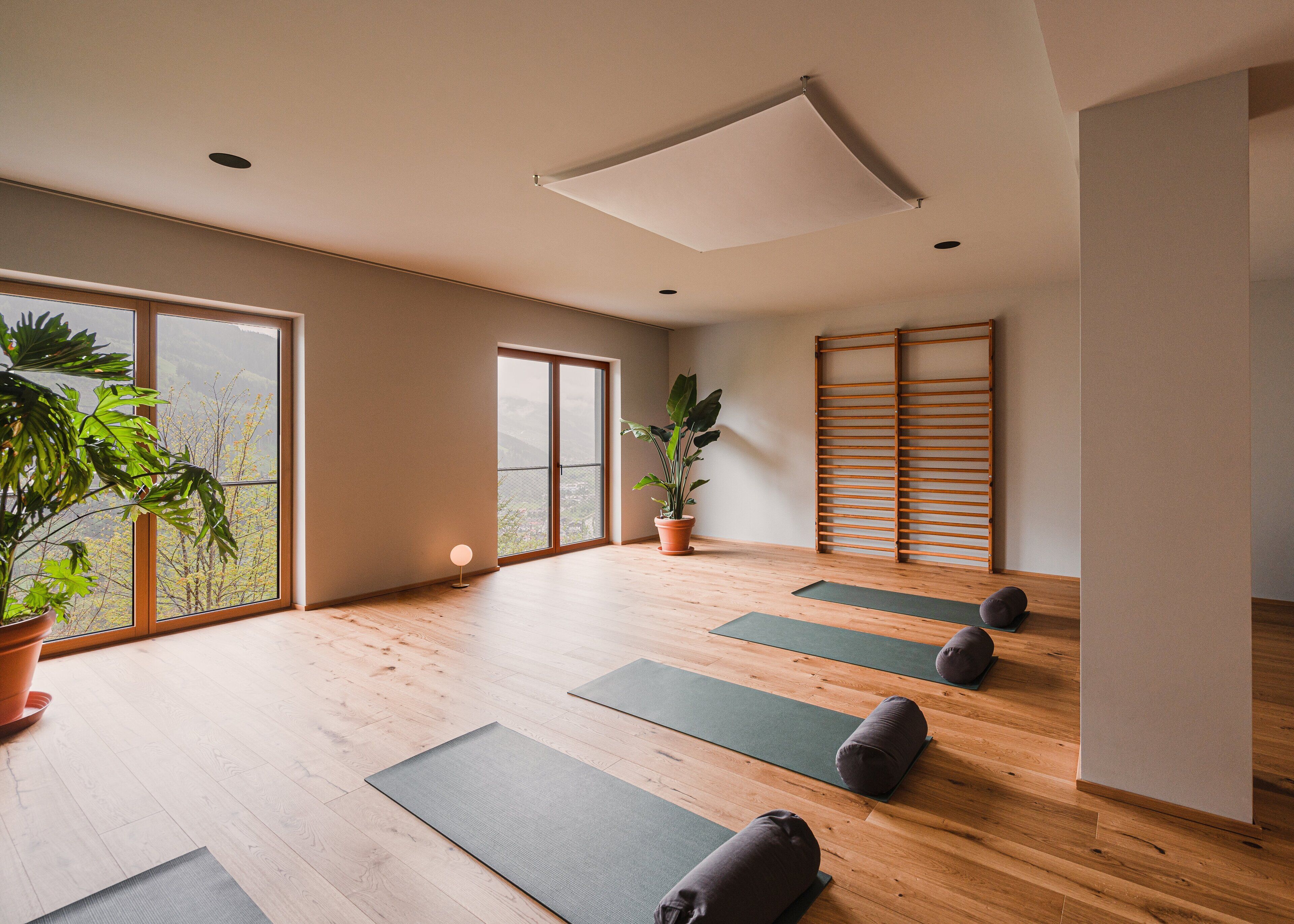 A spacious room with large windows, wooden flooring, and yoga mats arranged for practice.
