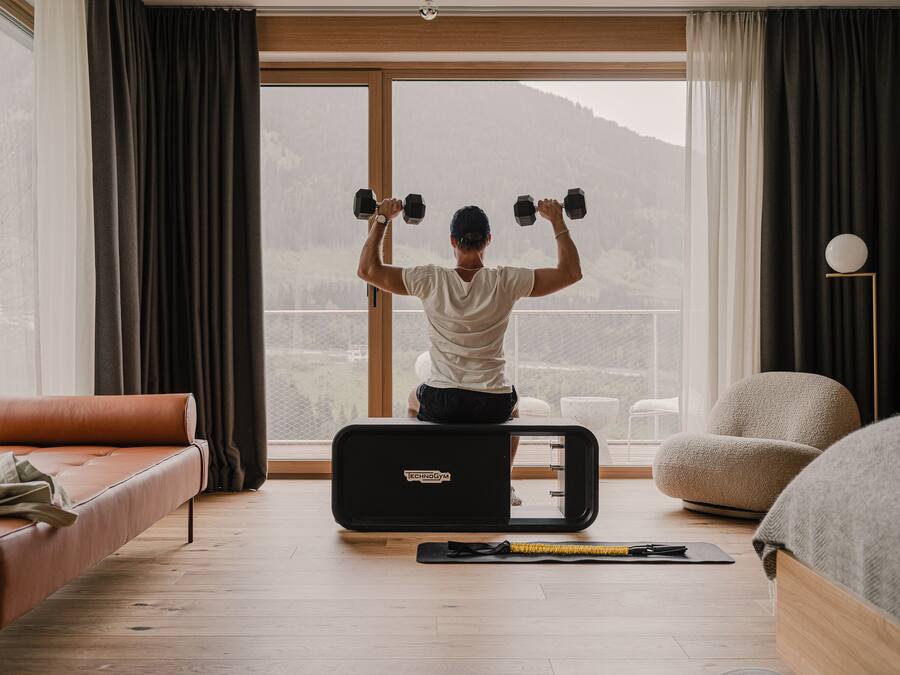 A person exercising with dumbbells in a room with a large window, a sofa, and a treadmill.
