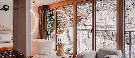 A modern bathroom with a freestanding bathtub, a wooden vanity, and a large window offering a view of a snowy landscape.