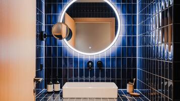 Un baño con un espejo grande, paredes de azulejos azules y un lavabo blanco.