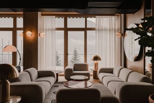 Ein modernes Wohnzimmer mit einer Sofagarnitur, einem Couchtisch und Blick auf eine verschneite Landschaft durch große Fenster.