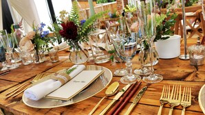 A wooden table set with gold cutlery, clear glassware, and floral centerpieces. - leleshwa inn (Kitengela)