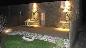 A stone building with a small patio area, a white table and chair, and a planter with plants. - Gite Andrée, 800m from the beach in Pirou, garden, terrace, wifi, wood stove (Pirou)