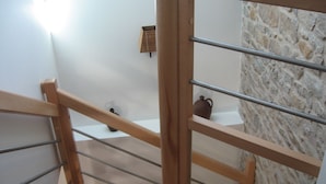 A wooden staircase with metal railings leading to a bathroom with a stone wall and a small shelf with a ceramic pot. - Gite Andrée, 800m from the beach in Pirou, garden, terrace, wifi, wood stove (Pirou)