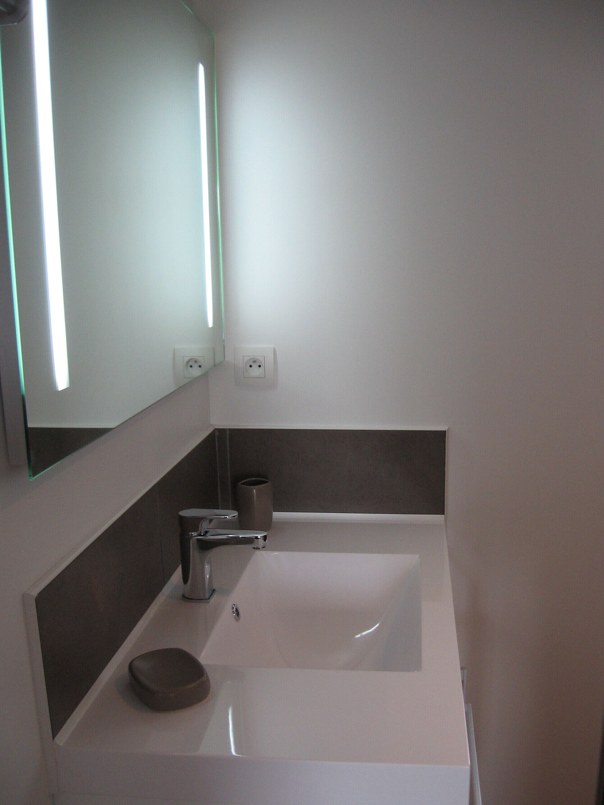 Un baño moderno con un lavamanos blanco, un espejo y una luz empotrada en la pared.
